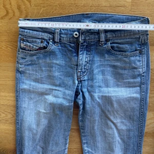 Blå lågmidjade bootcut jeans diesel - Säljer ett par snygga blå bootcut jeans med klassisk femficksdesign. Jeansen har en bekväm passform och är perfekta för en avslappnad stil. De har en dragkedja och knapp framtill. Liten fläck längst ner på byxan se bild 4. Storlek W28 passar s-xs. Se bild för mått!