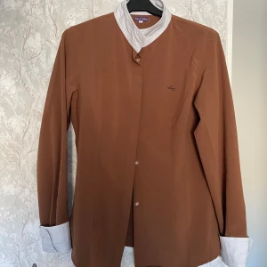 Brun rid skjorta från Equi-Theme - Väl använd men i väldigt bra skick. Har tvättats och har inget spår av häst på sig. Väldigt skön tröja och perfekt för tränings tävlingar eller bara vid lite finare tillfällen i stallet! Köptes för ca 600kr så väldigt prisvärd skulle jag säga.