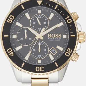 Svart och guld klocka från Hugo Boss - En helt ny oöppnad Original Hugo boss klocka.  Jag skickar gärna video om så önskas.  Material & Utförande Tillverkare: Hugo Boss Modell: 1513974 Rek. pris 5 298 kr  Serie: Energy Typ: Herrklocka, Dress / Sportmodell Diameter: Ø 44.00 mm Tjocklek: 10.50 mm Boett: Borstat/polerat stål Baksida boett: Solid Armband: Borstat och polerat stål gulguldtonat stål Urtavla: Grå med självlysande markeringar indexmarkeringar, självlysande visare Spänne: Viklås i stål Glas: Mineral Bezel (ring): Stål gulgul