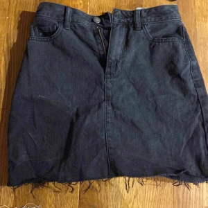 Svart jeanskjol från Hollister - Snygg svart jeanskjol från Hollister med rå kant och klassisk femficksdesign. Kjolen har en dragkedja framtill och är perfekt för en avslappnad stil. Passar bra till både sneakers och boots.