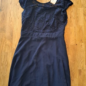Mörkblå spetsklänning från NLY Eve - Elegant mörkblå klänning från NLY Eve med spetsdetaljer på överdelen och korta ärmar. Perfekt för en stilfull kväll. Klänningen har en smickrande passform och en dragkedja i ryggen.