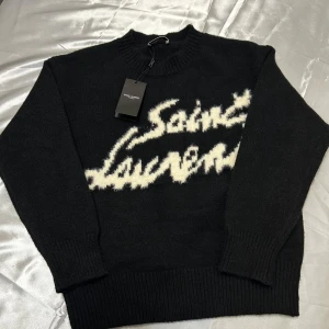 Svart tröja från Saint Laurent - Snygg svart tröja från Saint Laurent med vit text på bröstet. Tröjan har långa ärmar och en rund halsringning. Perfekt för en stilren look.