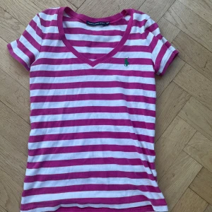 Rosa och vit randig t-shirt från Ralph Lauren - Säljer en snygg rosa och vit randig t-shirt från Ralph Lauren. Den har en v-ringad hals och korta ärmar med det klassiska gröna logotypen på bröstet. Perfekt för våren eller sommaren💕 Priset kan diskuteras🥰