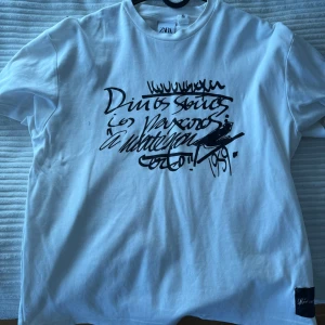 Vit t-shirt från Zara med tryck - Säljer en vit t-shirt från Zara med ett coolt svart grafiskt tryck på framsidan. Perfekt för en avslappnad stil. T-shirten har en klassisk rund hals och korta ärmar.