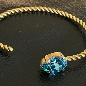 Caroline Svedbom – Classic Rope Bracelet (Gold turkois) - Caroline Svedbom Classic Rope Bracelet Gold Elegant guldarmband med en stor, gnistrande blå sten i centrum. Armbandet har en tvinnad design som ger en unik och stilren look. Perfekt för att lägga till en touch av färg och elegans till din outfit.