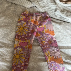 Färgglada leggings med elefantmönster från Lindex - Säljer ett par färgglada leggings från Lindex med ett lekfullt mönster av elefanter, blommor och moln i rosa, lila och orange nyanser. Perfekta för barn i åldern 4-5 år. Tillverkade i mjukt och bekvämt material. På sista bilden visas små fläckar som jag är lite osäker på om dem går bort därav priset