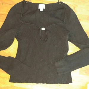 Svart ribbad tröja från H&M - Snygg svart ribbad tröja från H&M med en unik detalj framtill. Tröjan har långa ärmar och en stilren design som passar perfekt till olika tillfällen. Perfekt för dig som vill ha något enkelt men ändå speciellt.