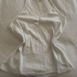 Vitt linne Gina Tricot -  vit linnetopp från Gina Tricot. Toppen har en enkel design med smala axelband och en lätt rynkning vid bysten. Perfekt för varma dagar eller som ett basplagg i garderoben. Knyt band 