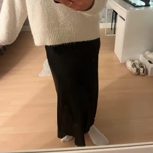 Svart långkjol - Snygg svart satin kjol. Perfekt för att matcha med en stickad tröja eller en elegant topp. Kjolen har en klassisk design som passar till många olika stilar.