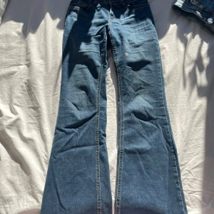Blå bootcut jeans från Lindex - Snygga blå bootcut jeans från Lindex. De har en klassisk femficksdesign och är perfekta för en avslappnad stil. Jeansen har en bekväm passform och är tillverkade i ett slitstarkt denimtyg.