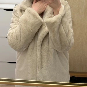 Beige pälsjacka från NA-KD - Aldrig använd etiketten sitter på! Säljer en supermjuk och fluffig beige pälsjacka från NA-KD. Jackan har en elegant krage och stängs med knappar framtill. Perfekt för att hålla sig varm och stilren under kyliga dagar. 🧥✨