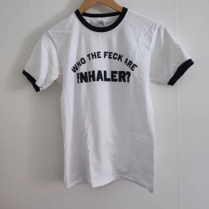 Inhaler t-shirt  - Säljer en vit t-shirt från bandet Inhaler med svart text 'WHO THE FECK ARE INHALER?' på framsidan. T-shirten har svarta kanter vid hals och ärmslut. Köpt via deras hemsida för några år sen. 