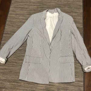 Randig kavaj - Snygg randig kavaj i svart och vit med klassisk krage och långa ärmar. Perfekt för en stilren look. Kavajen har två fickor framtill och en elegant passform.