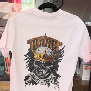 Vit t-shirt med dödskalletryck - Cool vit t-shirt med ett stort tryck av en dödskalle med krona och texten 'Mighty Things' på baksidan. Perfekt för en edgy look.