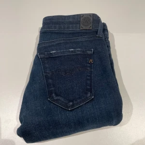 Mörkblå jeans från Replay - Snygga mörkblå jeans från Replay Hyperflex med en klassisk femficksdesign. De har en knappgylf och är perfekta för en stilren look. Passar bra till både vardag och mer uppklädda tillfällen.
