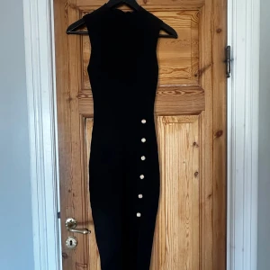 Svart ribbad klänning från Giorgia - Snygg svart ribbad klänning från Giorgia med eleganta knappar längs sidan. Klänningen är ärmlös och har en stilren design som passar perfekt för olika tillfällen. Perfekt för dig som vill ha en chic och tidlös look.