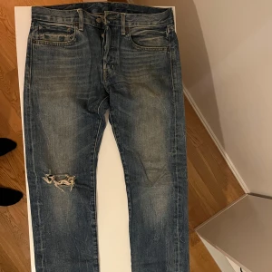 Blå jeans från Ralph Lauren - Snygga blå jeans från Ralph Lauren med slitna detaljer och en cool vintage-look. De har en klassisk femficksdesign och en patch med amerikansk flagga på baksidan. 31/34