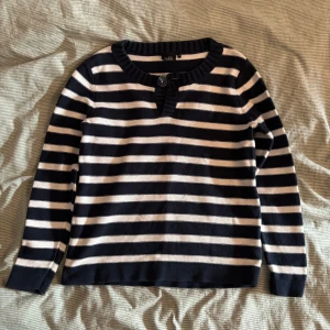 Randig tröja från Isolde - Säljer en snygg randig tröja från Isolde i svart/marinblått och vit. Tröjan har långa ärmar och en knappdetalj vid halsen. 