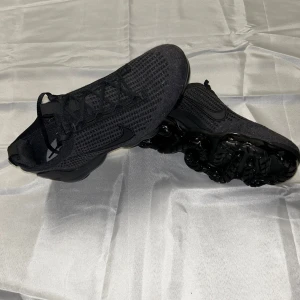 Svarta Nike Vapormax sneakers - Snygga svarta Nike Vapormax sneakers med en modern design och luftig ovandel. Skorna har en unik sula med synliga luftkuddar för extra komfort och stil. Perfekta för både träning och vardagsbruk.
