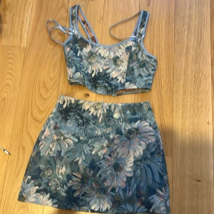 Blommig kjol med matchande topp XS - Snygg blommig kjol i blå och rosa toner med matchande topp. Kjolen är kort och har ett vackert blommönster som ger en romantisk känsla. Toppen har smala axelband och en croppad passform. Perfekt för en somrig look!