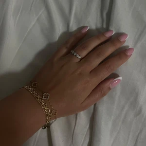 Guldarmband med fyrklöverdesign - Elegant guldarmband med fyrklöverdesign. Armbandet har en tunn kedja med små fyrklöverdetaljer, varav en är dekorerad med glittrande stenar. Perfekt för att lägga till en touch av lyx till din stil. Den är köpt i Spanien 🇪🇸 använd 2-3 gånger.