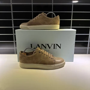 Beige sneakers från Lanvin - Snygga beige sneakers från Lanvin med en stilren design. Skorna har snörning och en vit sula som ger en modern touch. Tillverkade i skinn för en lyxig känsla. Perfekta för en avslappnad men elegant stil.