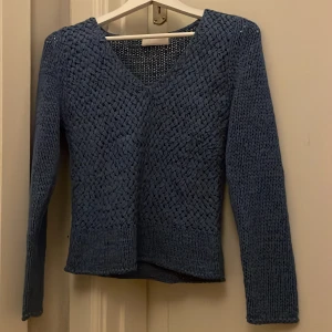 Blå stickad tröja från Oui Moments - Säljer en snygg blå stickad tröja från Oui Moments. Tröjan har en v-ringad design och långa ärmar, perfekt för kyligare dagar. Den har ett unikt flätat mönster som ger en stilren look. 