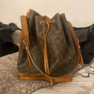 Lv noe bag - Säljer en klassisk brun axelväska från Louis Vuitton med det ikoniska monogrammönstret. Väskan har justerbara axelremmar och snygga läderdetaljer. Den har lämnats in hos en bra skräddare som lagade fästet på axelremmen💕den har många år kvar och de går att rusta upp. Kom för fler bilder
