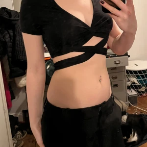 Svart omlott topp - Snygg svart omlott topp med korta ärmar och unik design med band som korsar magen. Oklart vart jag köpt den, troligen second hand. Pris kan diskuteras 