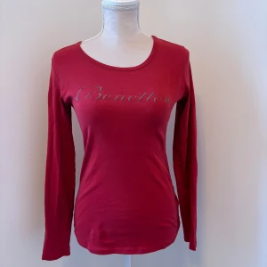 Röd långärmad topp från Benetton - Snygg röd långärmad tröja från Benetton. Mjuk o skön o ganska tunn! Vissa delar av loggan på framsidan sitter lite löst.