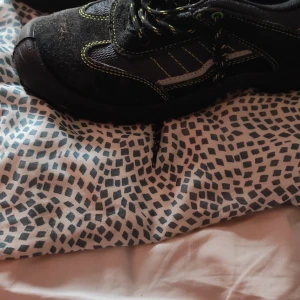 Svarta arbetsskor med gröna detaljer - Säljer ett par svarta arbetsskor med gröna detaljer och snörning. Skorna har en robust design med förstärkt tå och är perfekta för arbete där extra skydd behövs.