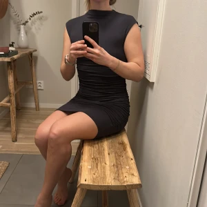 Svart tight klänning - Snygg svart tight klänning med rynkade detaljer på sidorna. Den är ärmlös och har en kort längd som ger en stilren look. Perfekt för en kväll ute eller en speciell tillställning.