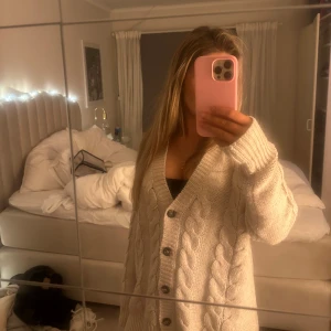 Beige stickad kofta med knappar - Mysig beige stickad kofta med kabelstickat mönster och knappar framtill. Perfekt för kyliga dagar och ger en avslappnad look. 