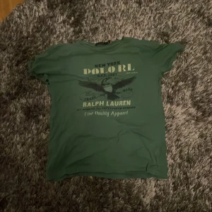 Grön t-shirt från Ralph Lauren, Custom slim fit - Säljer en grön t-shirt från Ralph Lauren med tryck på framsidan. T-shirten har korta ärmar och är i en slim fit passform. Perfekt för en avslappnad stil. Köpt för 1399. Bra skick men använd. Storlek M men passar S