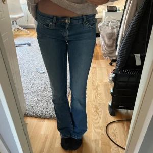 Blå bootcut jeans - Snygga blå bootcut jeans med klassisk femficksdesign och knappgylf. Perfekta för en avslappnad stil. De har en lätt slitning vid fållen som ger en cool look.