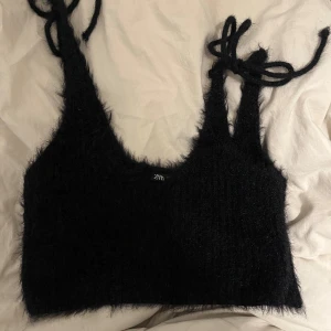 Svart fluffig topp från Zara - Säljer en svart fluffig topp från Zara med knytband vid axlarna. Toppen är ärmlös och har en mjuk, lurvig textur som ger en unik look. Perfekt för att lägga till en touch av stil till din garderob.