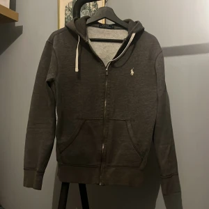 Grå hoodie från Ralph Lauren - Säljer en stilren grå hoodie från Ralph Lauren i okej skick 6/10. Stolek S. Inget är fel på hoodien förutom armbågarna men borsätt från det är den skick 8/10.