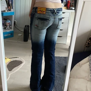 Blå jeans med broderade detaljer - Snygga blå jeans med broderade blommor vid fickorna och en cool tvättad look. De har en bootcut-stil och låg midja, perfekt för en avslappnad stil. Märket 'Success' syns på etiketten baktill. 