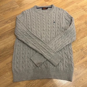 Morris tröja - Säljer en stilren grå kabelstickad tröja från Morris i 100% Pima Cotton. Tröjan har en klassisk rund hals och långa ärmar med ribbade muddar. Perfekt för kyligare dagar och ger en tidlös look.