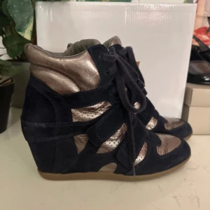 Svarta och bronsfärgade kilklackar  - Snygga kilklack i svart mocka med bronsfärgade detaljer. Skorna har en kilklack och snörning framtill för en cool look. Perfekta för att ge lite extra höjd och stil till din outfit.