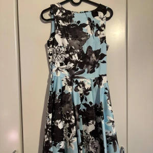 Blommig klänning från Closet London - Snygg ärmlös klänning från Closet London i en härlig ljusblå färg med stora svarta och vita blommor. Klänningen har en dragkedja i ryggen och en elegant passform som ger en fin siluett. Perfekt för sommarens alla tillfällen! 🌸