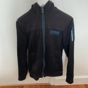 Hugo boss tröja  - Säljer nu en riktigt snygg Hugo boss tröja. Tröjan har snygga blå detaljer. Den är lite solblekt på luvan men inget som märks. Tveka inte om ni har några funderingar!