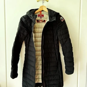 Fin svart äkta Parajumpers lång jacka lång modell Irene Hooded Down Jacket W Black stl XXS - Super fin jacka. Den är snygg och varm och säljes pga jag har många jackor.  Använd fåtal gånger (mindre än 10 gånger) i mycket bra skick hel och fin. Nypris 5799kr hos Skistar. Äkta parajumpers dunjacka.  Denna dunjacka från Parajumpers är lite längre i modellen och värmer gott med sin dunvaddering. Osynliga fickor med dragkedja och en stilren design gör dessutom jackan till ett klassiskt plagg som du kan ha länge.