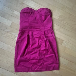 Rosa axelbandslös klänning - Snygg rosa axelbandslös klänning med en figurnära passform. Perfekt för en kväll ute eller en speciell tillställning. Klänningen har en hjärtformad urringning och en kort längd som ger en elegant look. Den är skitsnygg utanpå kostymbyxor