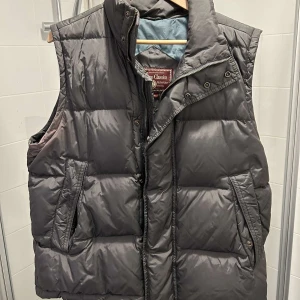 Grå dunväst från Marlboro Classics - Säljer en stilren grå dunväst från Marlboro Classics. Västen har en dragkedja och knappar framtill. Pris kan diskuteras 