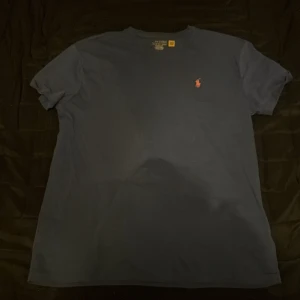 Blå t-shirt från Polo Ralph Lauren - Säljer en klassisk blå t-shirt från Polo Ralph Lauren med korta ärmar och en liten röd logga på bröstet. Perfekt för en stilren och avslappnad look.
