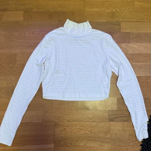 Vit ribbad polotröja - Säljer en stilren vit polotröja med ribbad struktur. Tröjan är croppad och har långa ärmar, perfekt för en trendig look. Passar bra till både jeans och kjol. 