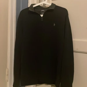 Svart tröja från Polo Ralph Lauren - Säljer en stilren svart tröja från Polo Ralph Lauren med zip vid halsen. Tröjan har långa ärmar och en liten broderad logotyp på bröstet. Perfekt för en klassisk och avslappnad look inför våren.                      Priset är förhandlingsbart ✅