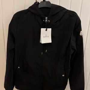 Moncler windbreaker  - Säljer nu denna snygga svarta vindjacka från Moncler för ett oerhört bra pris, Jackan har Moncler-logga på ärmen och en randig detalj i rött och vitt på huvan. Perfekt för blåsiga dagar. Den passar dig som är 180 och uppåt. Hör av er vid minsta fundering 🤔 