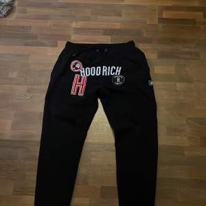 Säljer ett par svarta mjukisbyxor från Hoodrich med coola tryck och snörning i midjan. Perfekta för en avslappnad stil. Byxorna har en normal passform och är gjorda i ett mjukt material för extra komfort.